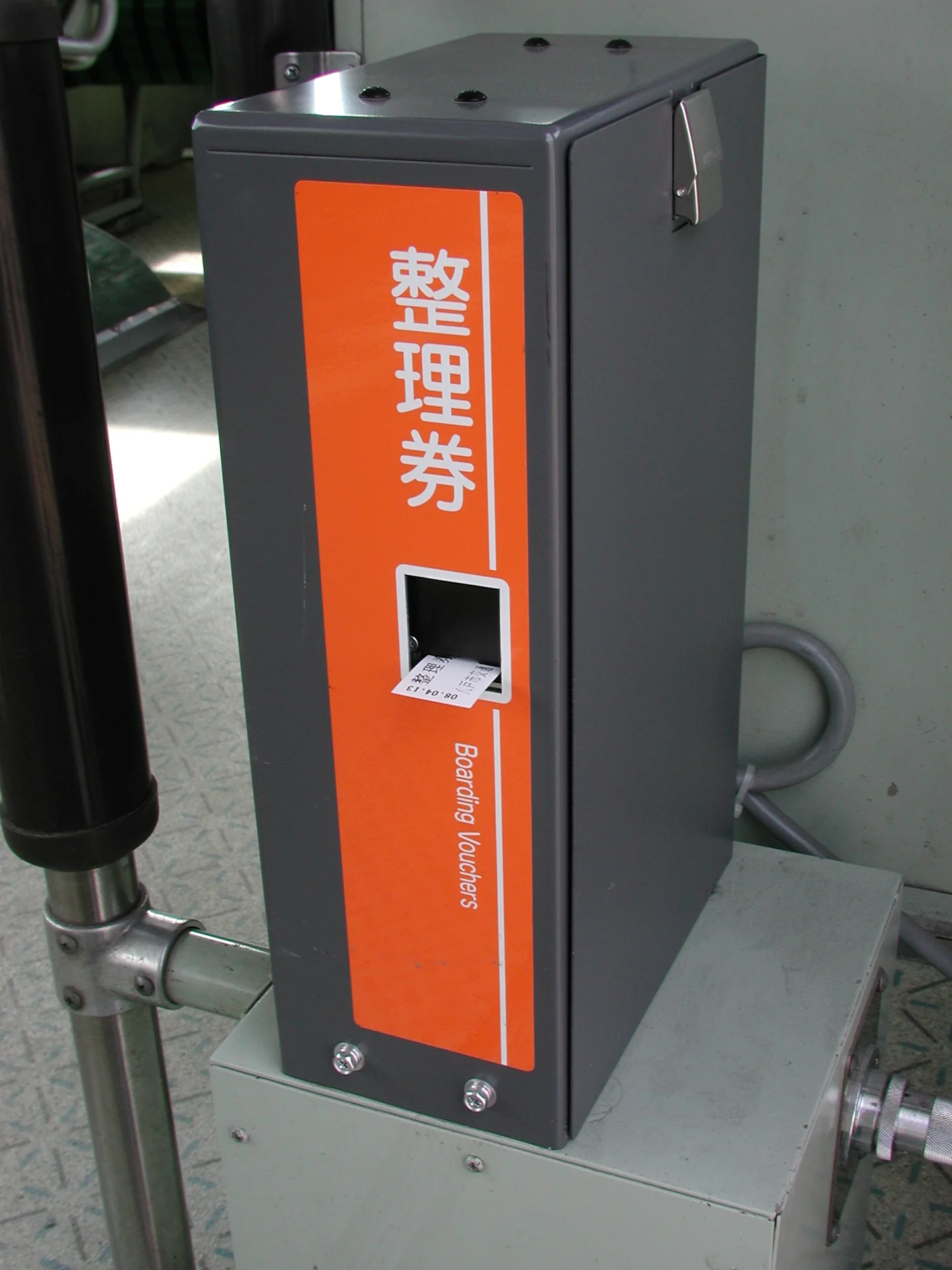 A numbered-ticket dispenser beside the boarding door of a Japanese regional bus